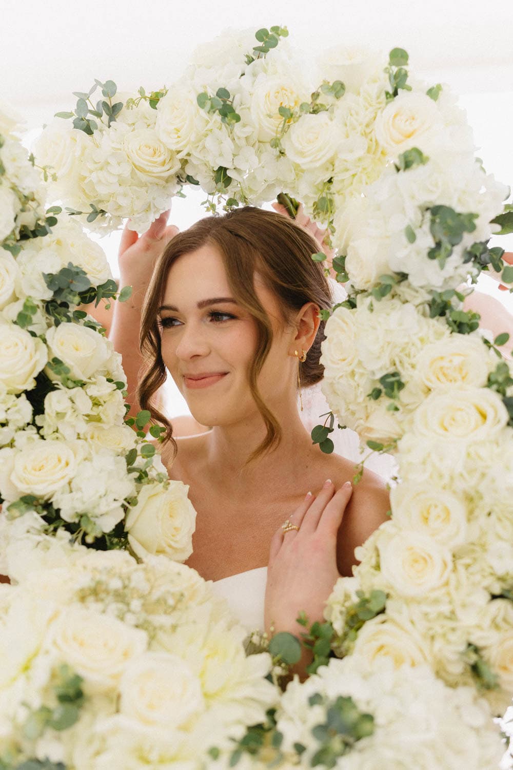 Bridal portrait surrounded by elegant white roses and greenery, showcasing beautiful floral arrangem.