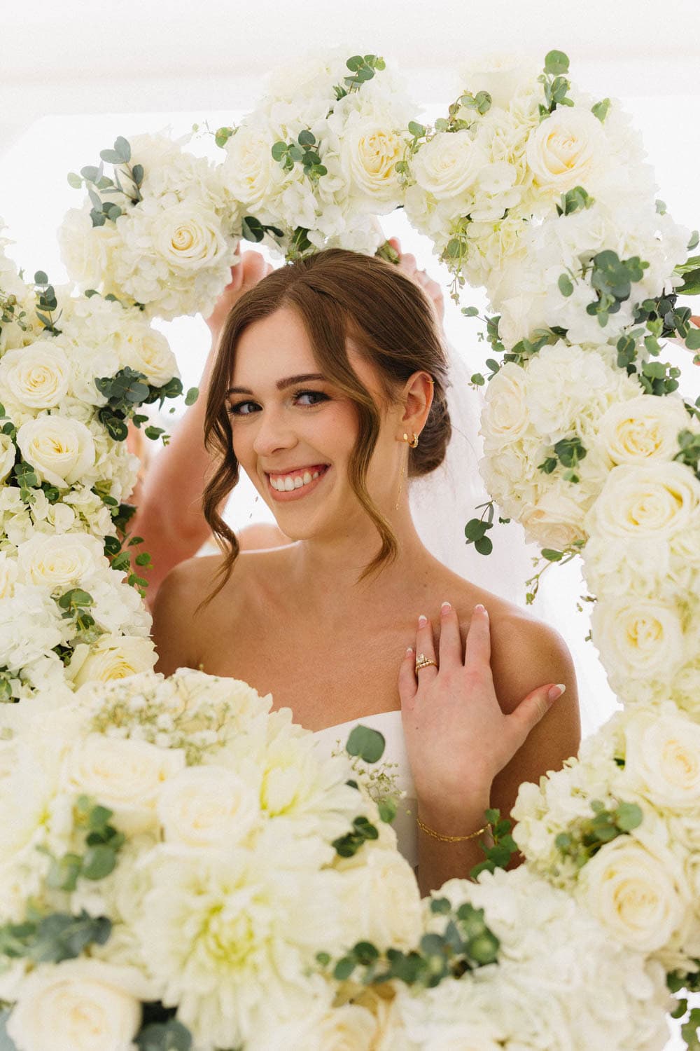 Beautiful bride surrounded by white roses and greenery, showcasing floral wedding decor.