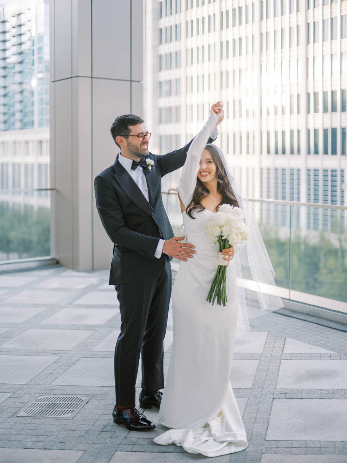 Elegant wedding couple celebrating with flowers in modern cityscape background.