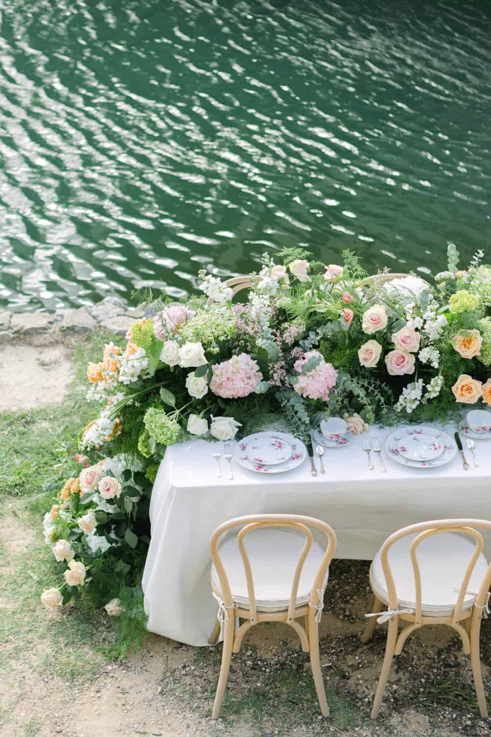 Elegant floral table setting with pastel roses and greenery by the water.