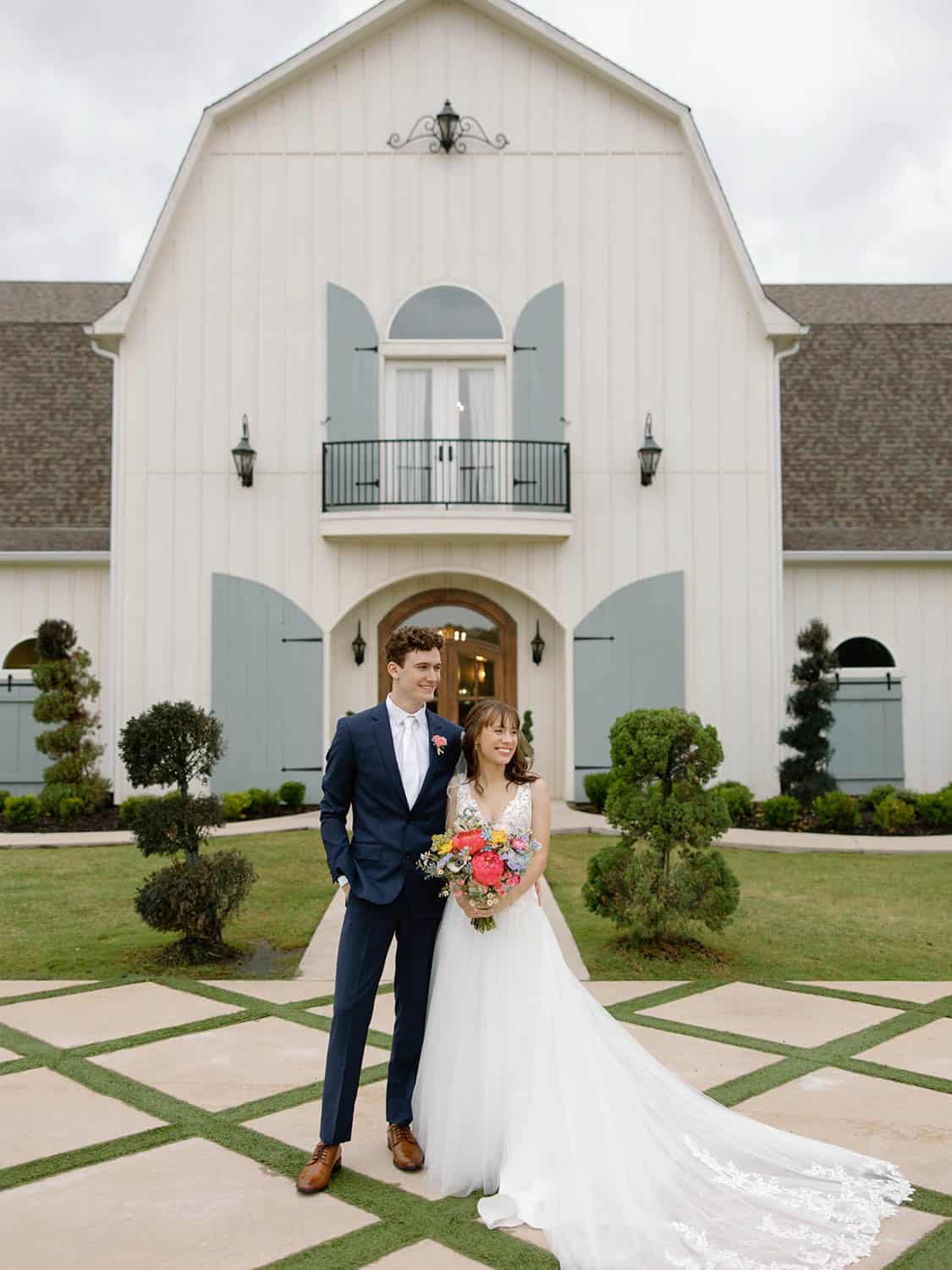 Beautiful wedding couple standing in front of Simply Blessed Flowers venue with floral bouquet.