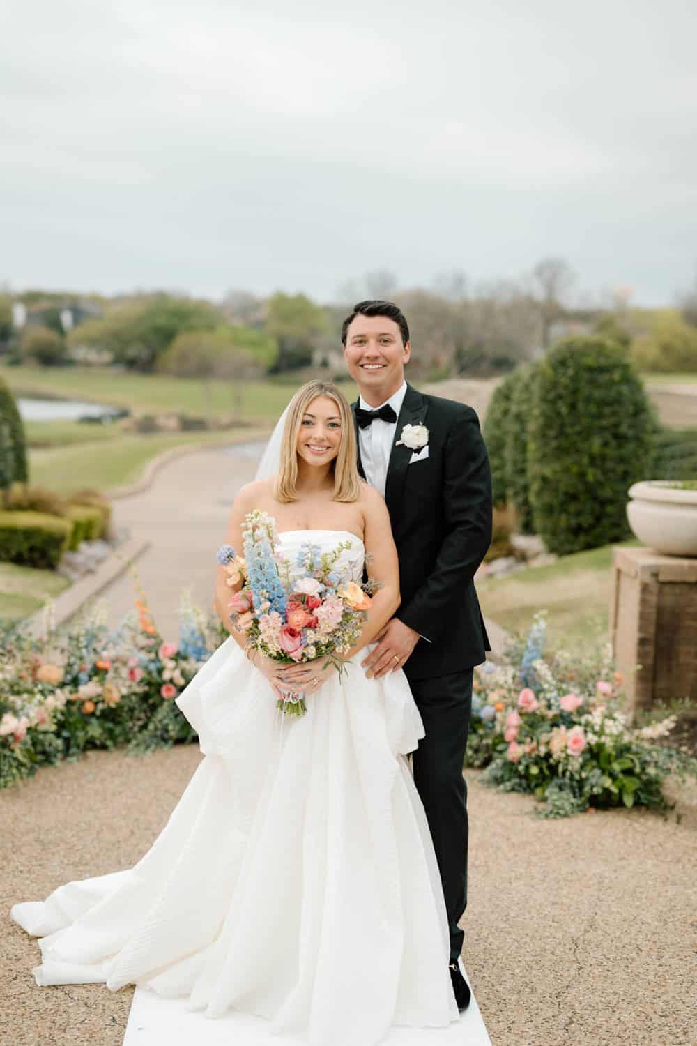 Bride holding a colorful bouquet, groom in tuxedo smiling.