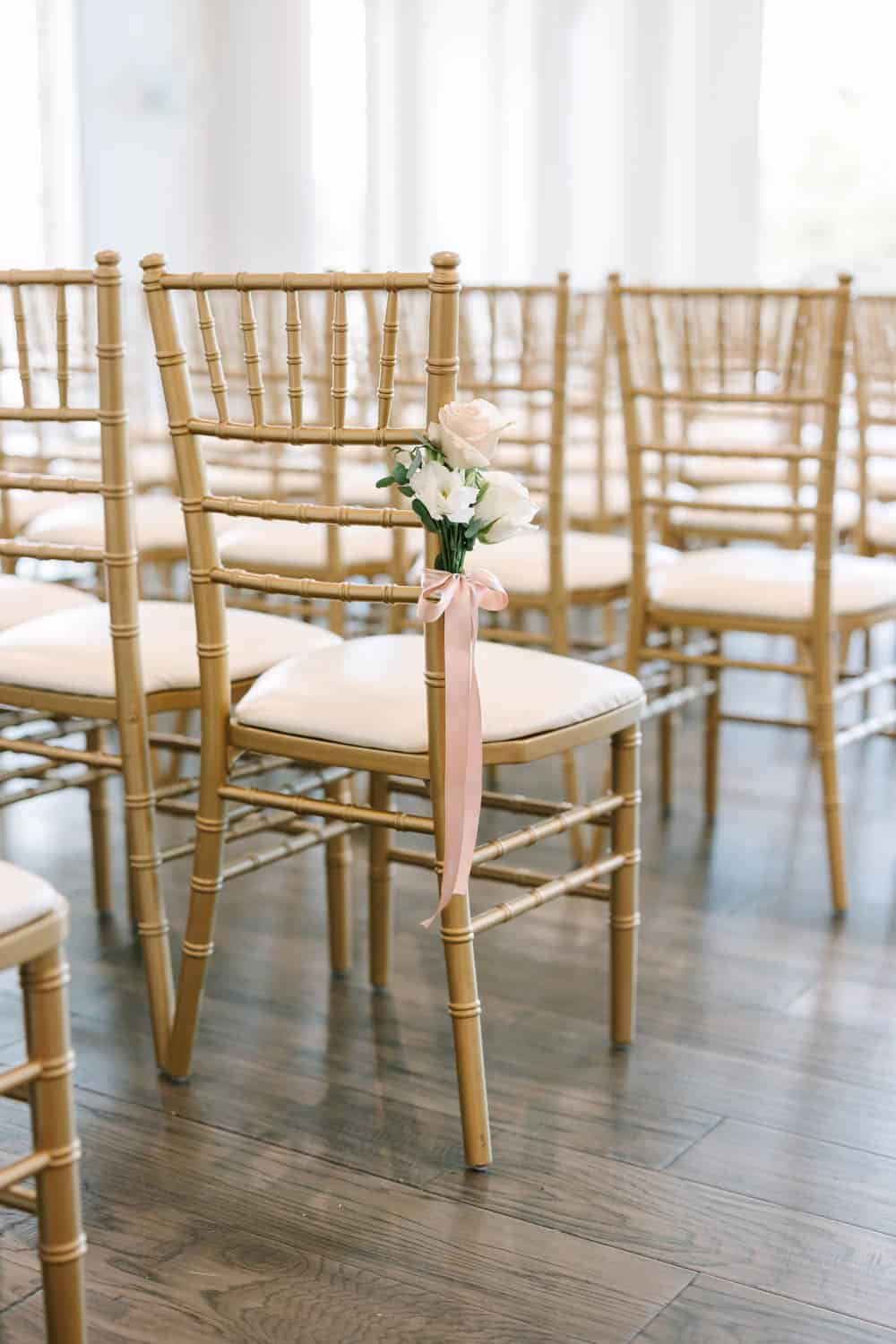 Elegant wedding chair with white flower arrangement and pink ribbon for event decor.
