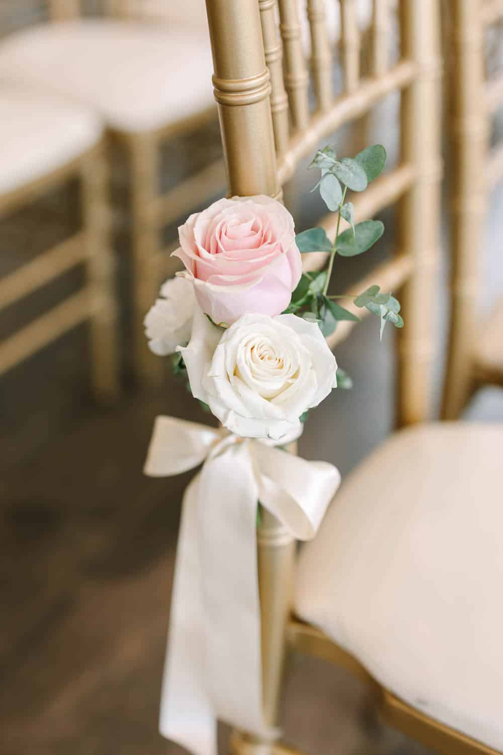 Beautiful pink and white roses with greenery adorn a gold chair for wedding decor.