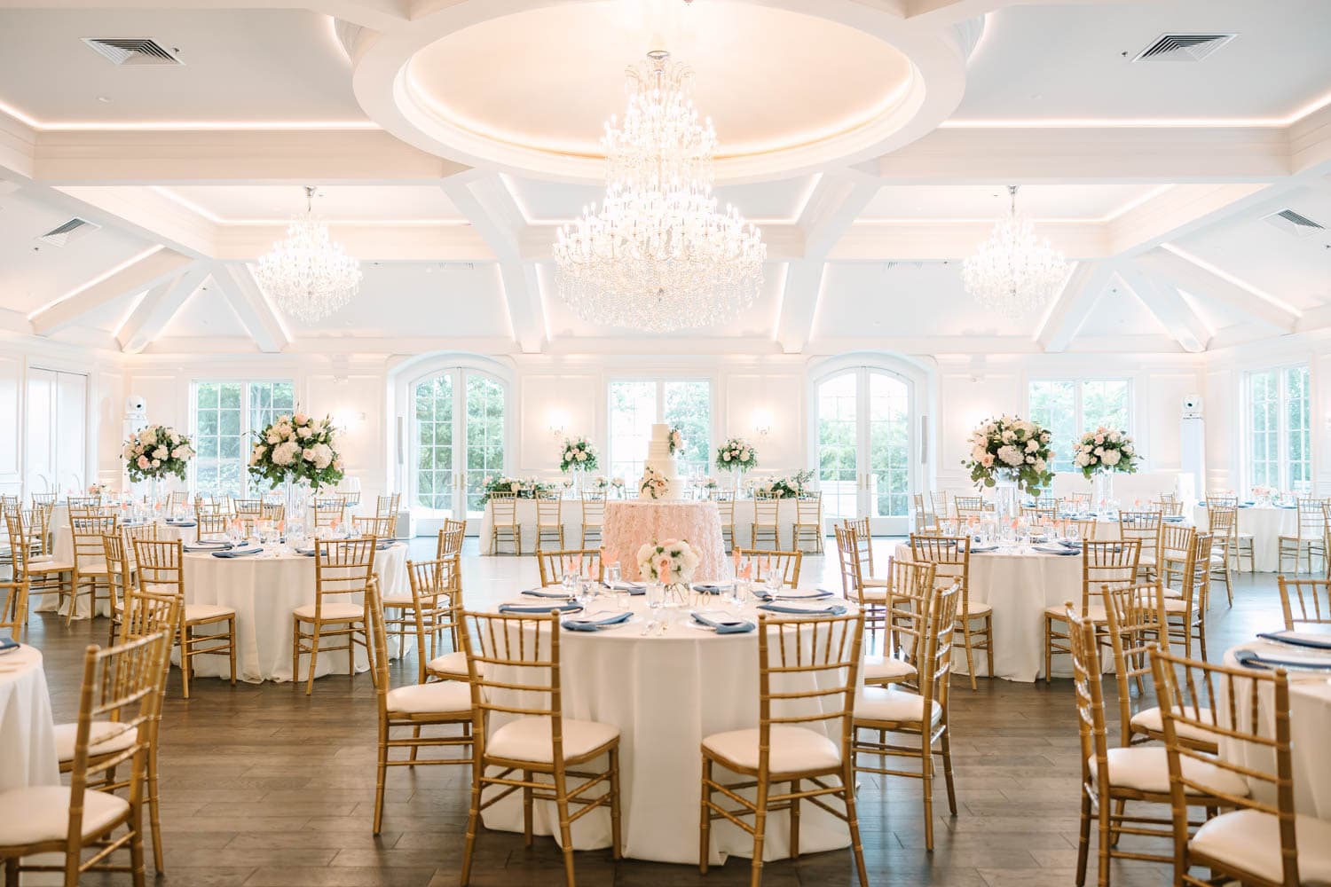 Elegant wedding reception with floral centerpieces and chandeliers in a bright, spacious venue.